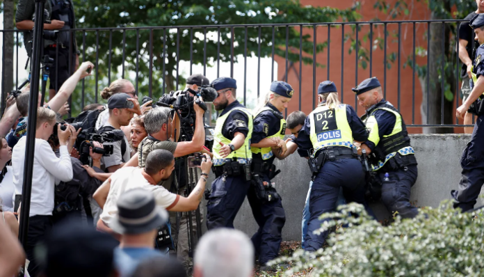 Police officers seen as protestors burn the Quran outside Stockholm's central mosque.