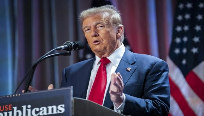 Donald Trump speaking at a podium with US flags in the background